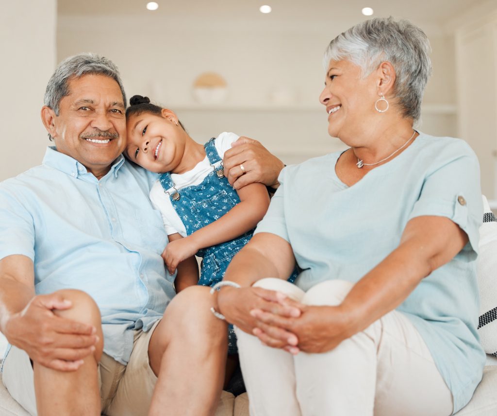 Two happy grandparents sitting on a sofa with their young granddaughter