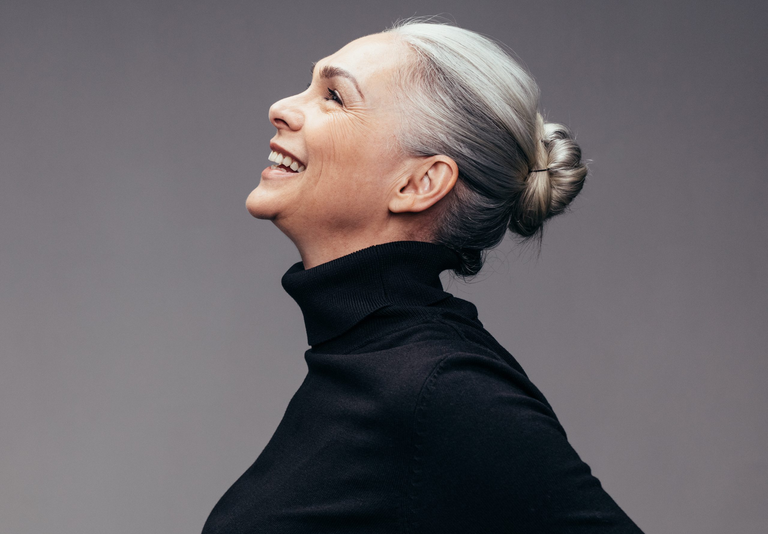 Side view of senior woman laughing on gray background