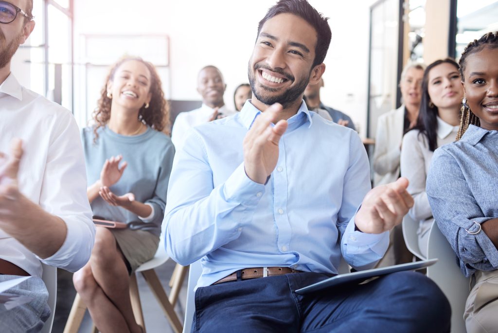 A group of professionals in a conference setting are applauding. A group of professional people at a conference, seminar or corporate workshop are sitting in chairs while applauding